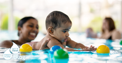 Mutter hält ihren Sohn im Wasser beim Babyschwimmkurs, das Kind spielt mit bunten Bällen