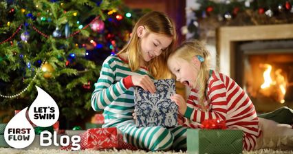 Zwei Kinder packen vor dem Weihnachtsbaum Geschenke aus